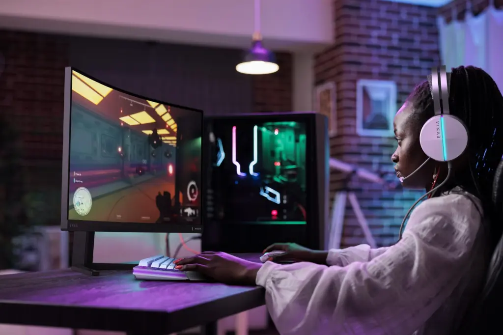 Joueuse sur PC gamer avec écran incurvé, casque gaming et setup RGB dans une chambre moderne